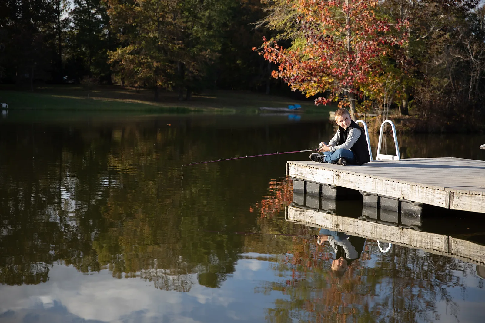 Boy fishing off the dock at the Orchid Hollow pond in autumn